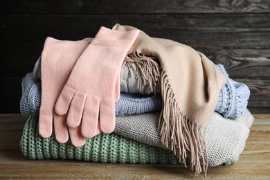 Photo of Stacked sweaters and gloves on wooden table, closeup. Autumn clothes