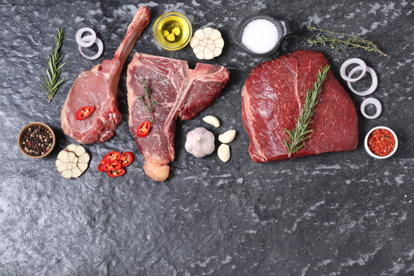 Photo of Fresh raw beef cuts and different spices on grey textured table, flat lay. Space for text