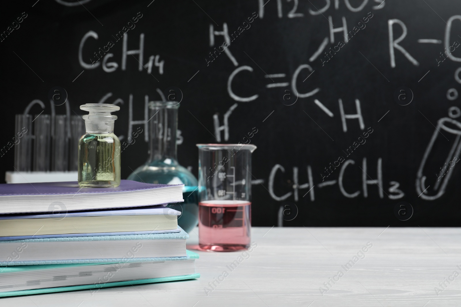 Photo of Laboratory glassware and school supplies on table against blackboard with chemical formulas