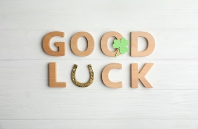 Photo of Phrase GOOD LUCK made of wooden letters and horseshoe on white table, flat lay