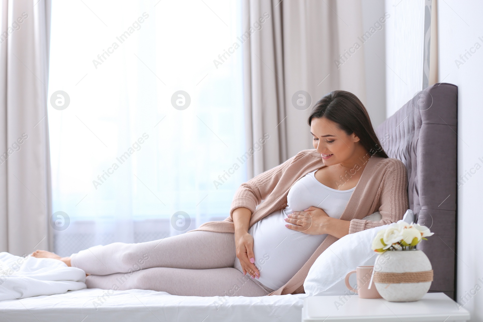 Photo of Young beautiful pregnant woman lying on bed and touching her belly at home