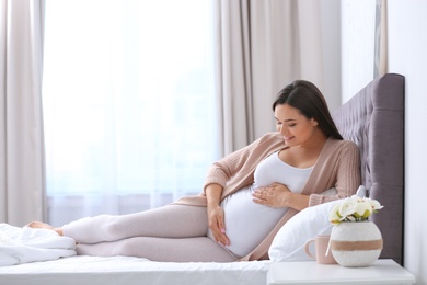 Photo of Young beautiful pregnant woman lying on bed and touching her belly at home