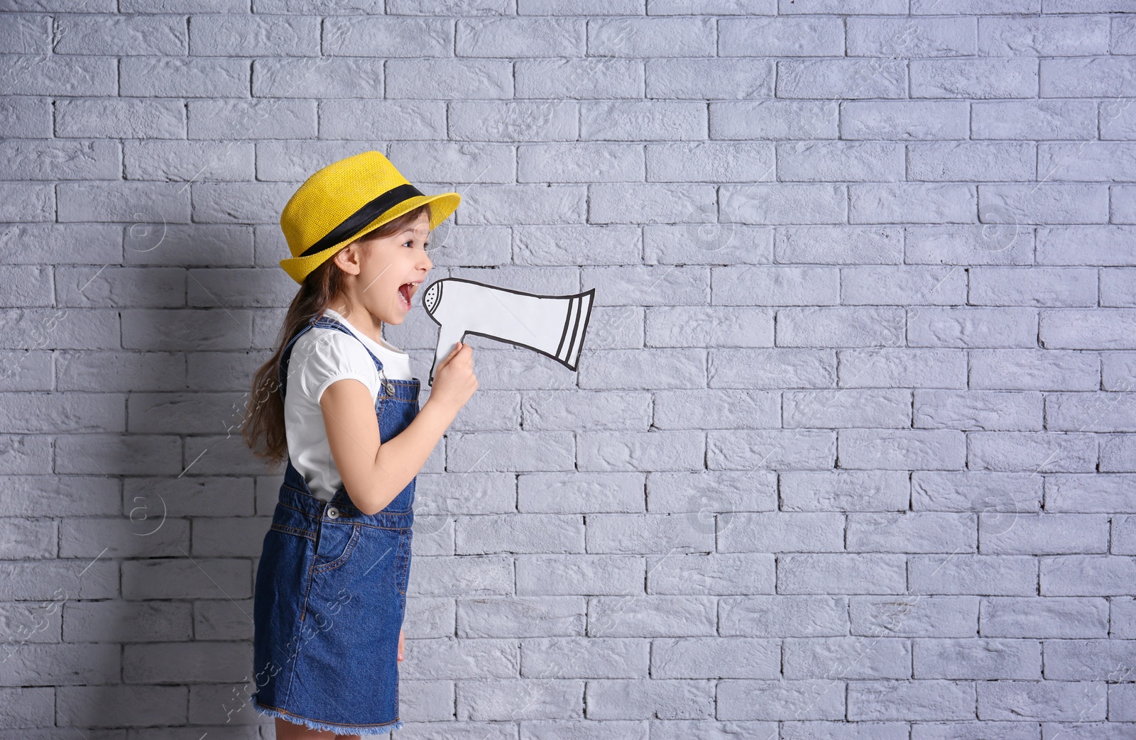 Photo of Adorable little girl with paper megaphone on brick wall background