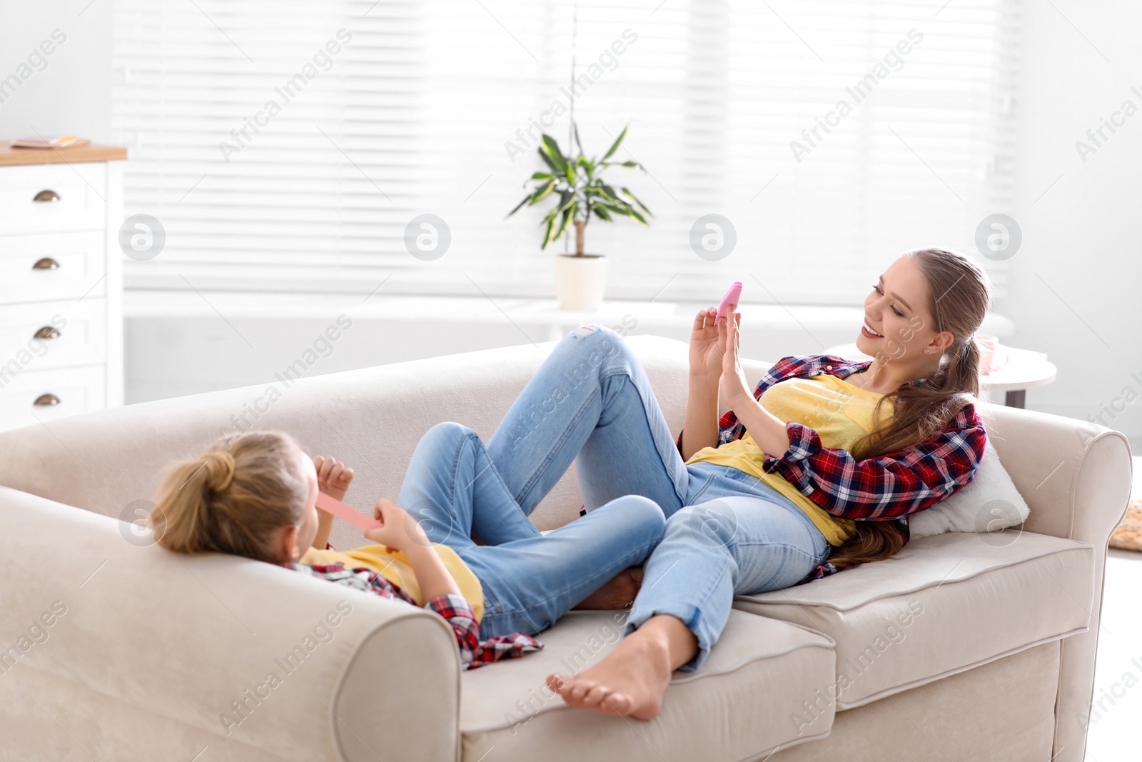 Photo of Happy mother and little daughter filing nails on sofa at home
