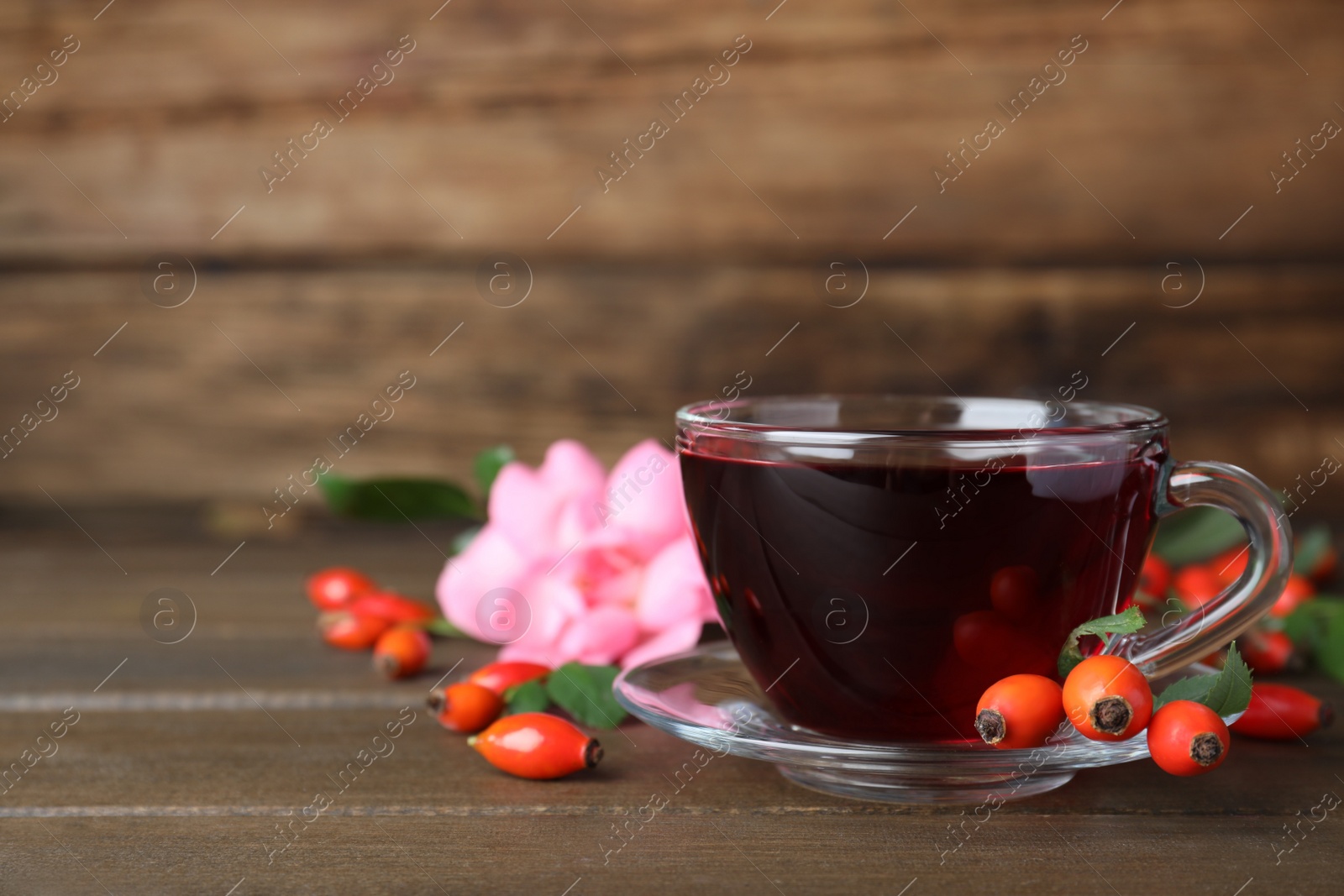 Photo of Aromatic rose hip tea and fresh berries on wooden table, space for text