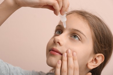 Photo of Adorable girl using eye drops on beige background, closeup