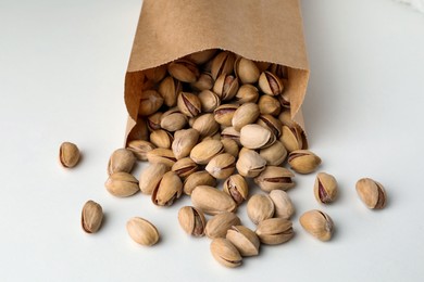 Photo of Overturned paper bag with pistachio nuts on white background