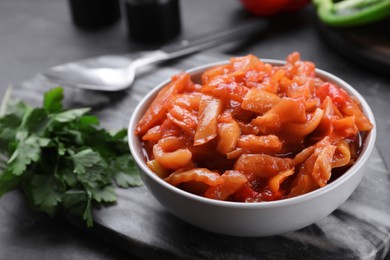 Delicious lecho with parsley in bowl on black table, closeup