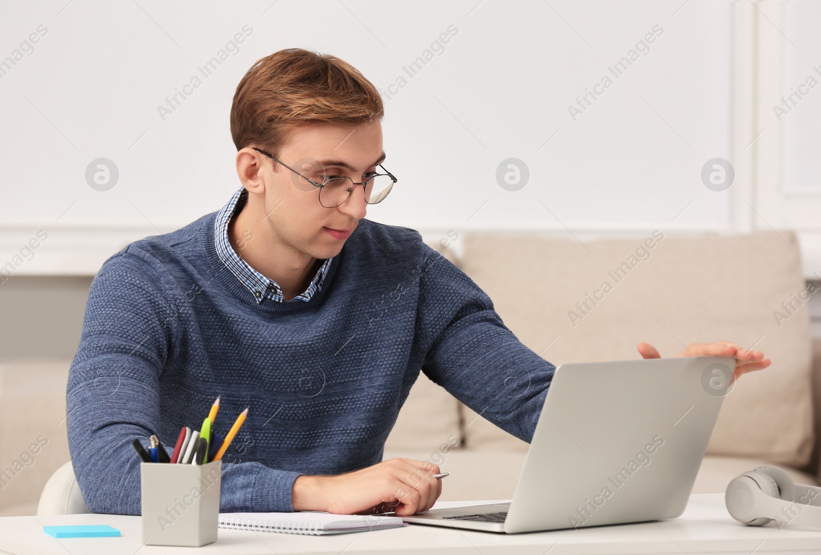 Photo of Young man with laptop writing in notebook at table indoors