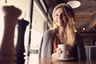 Young woman with cup of coffee at cafe in morning