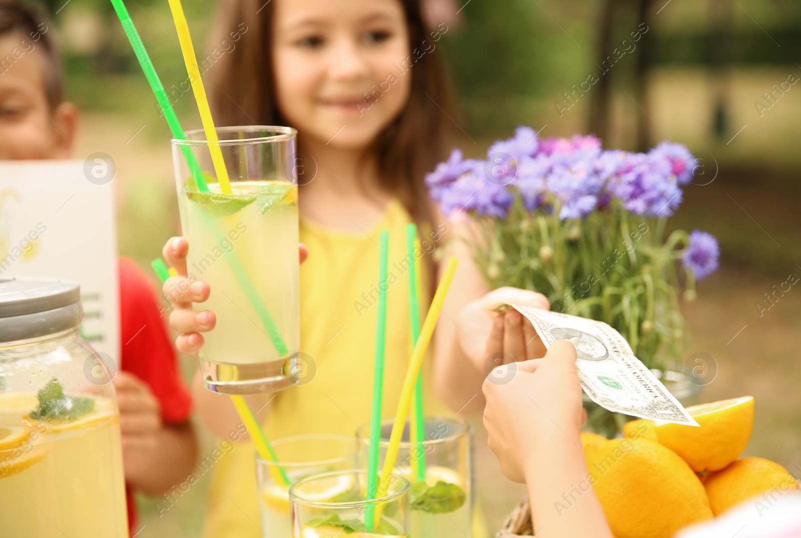 Photo of Little girl selling natural lemonade at stand in park