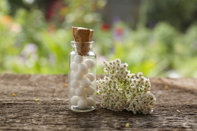 Photo of Bottle of homeopathic remedy and beautiful flowers on wooden table