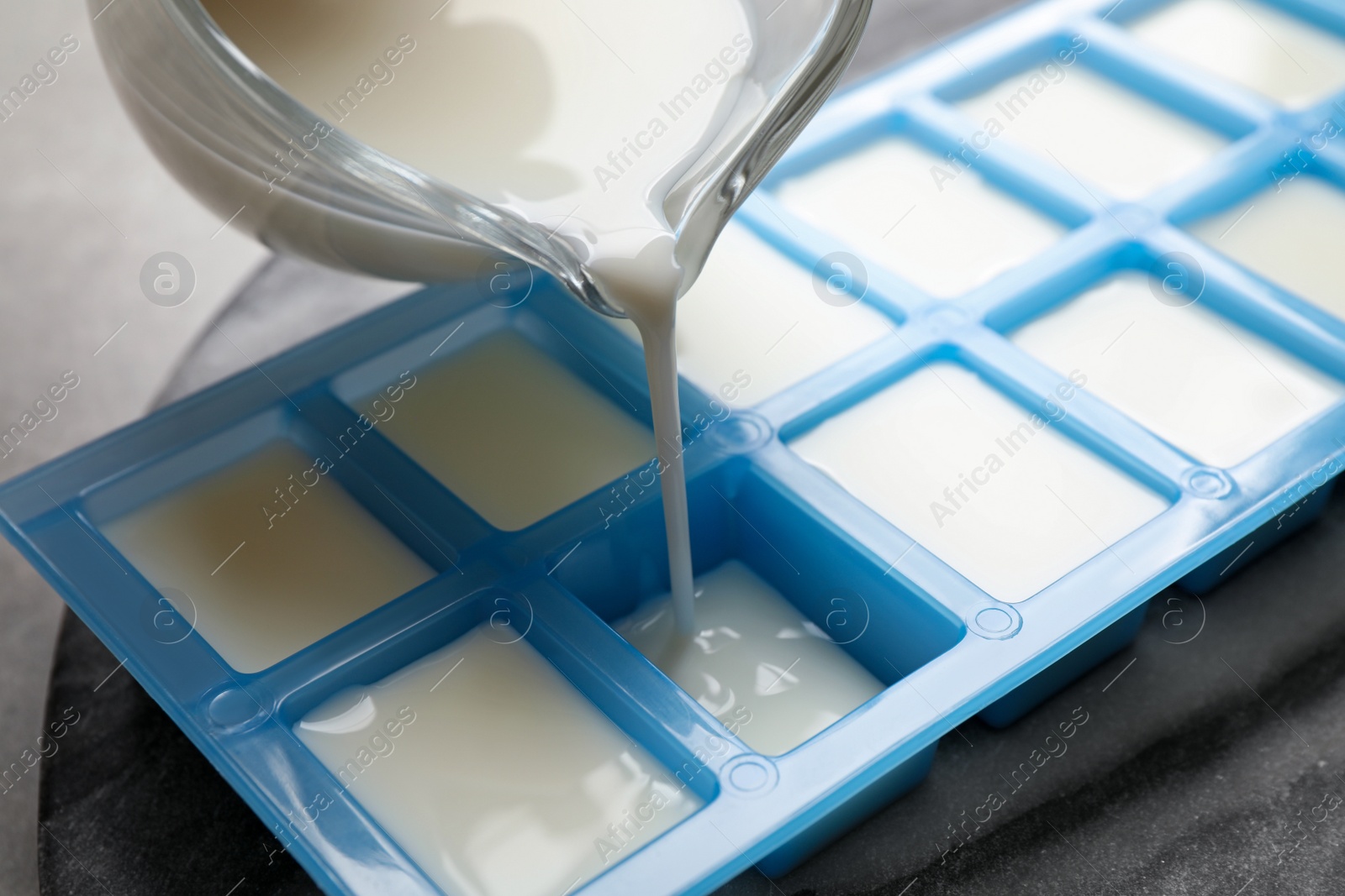 Photo of Pouring milk into ice cube tray at table, closeup