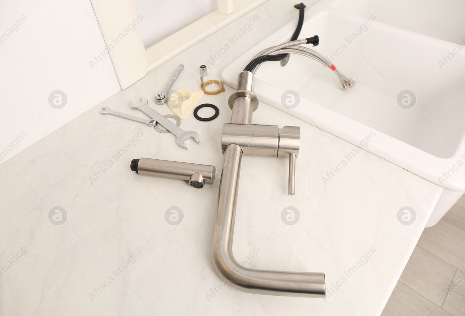 Photo of Plumber's tools and water tap ready for installation near sink on countertop in kitchen