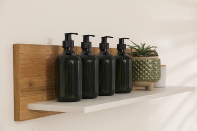 Photo of Bottles of hygiene products and houseplant on shelf in bathroom