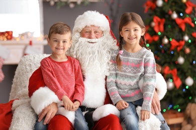 Photo of Little children sitting on authentic Santa Claus' knees indoors