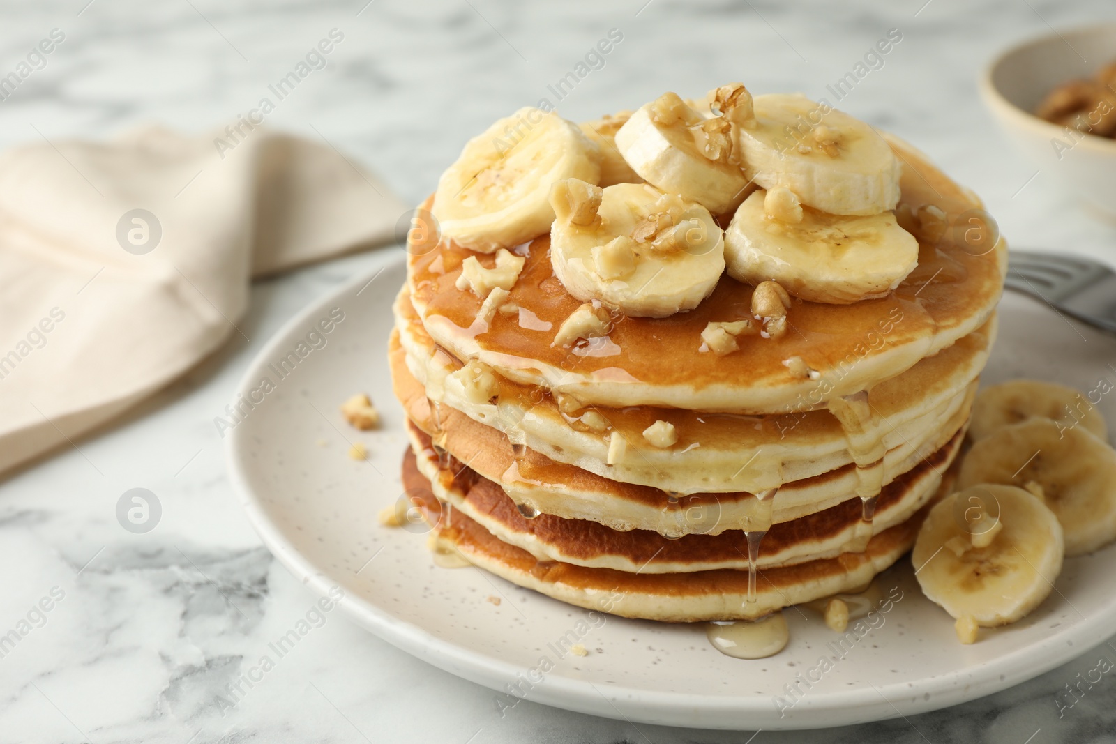 Photo of Delicious pancakes with bananas, walnuts and honey on white marble table, closeup