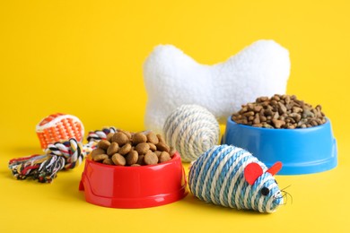 Photo of Feeding bowls and toys for pet on yellow background
