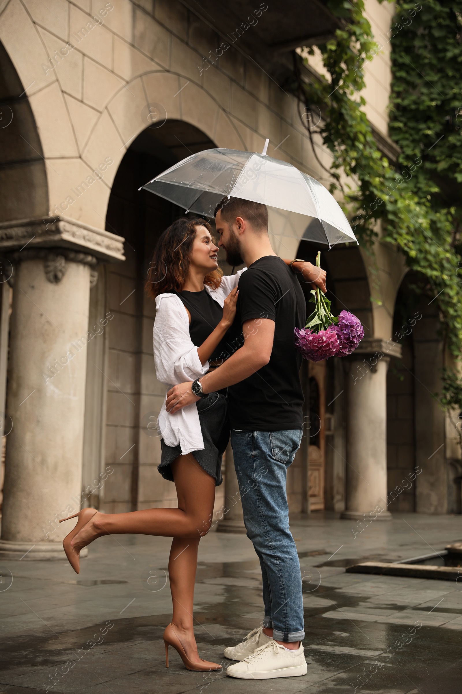 Photo of Young couple with umbrella enjoying time together under rain on city street