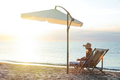 Photo of Woman with cocktail relaxing on deck chair at sandy beach. Summer vacation