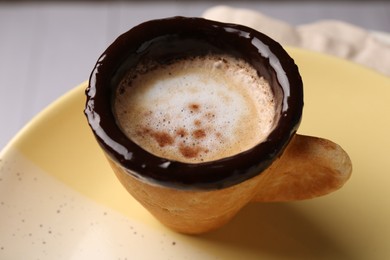 Delicious edible biscuit cup with coffee on plate, closeup