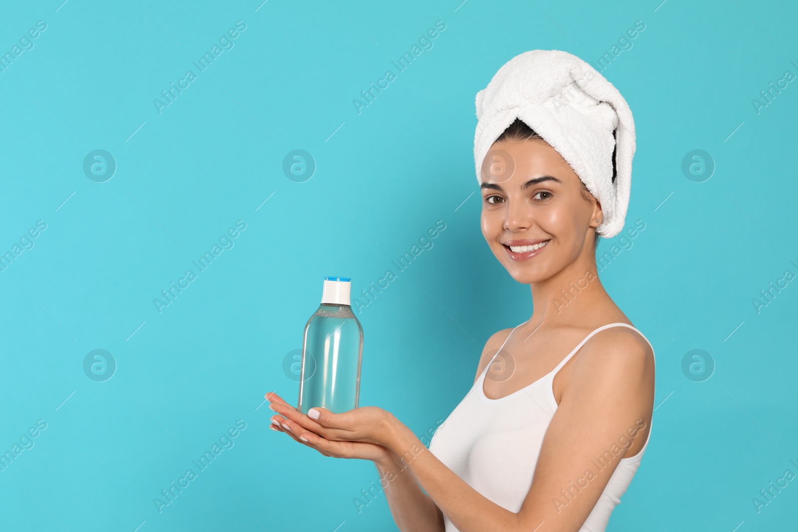 Photo of Young woman with bottle of micellar water on light blue background, space for text