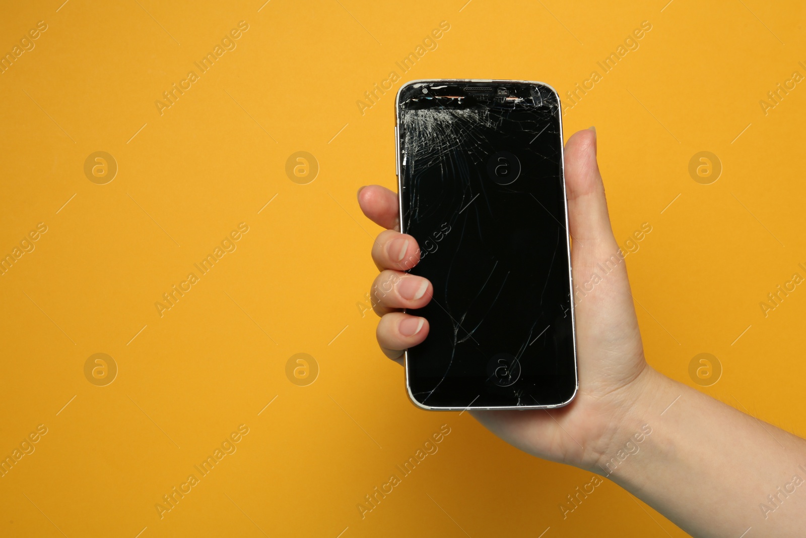 Photo of Woman holding damaged smartphone on orange background, closeup with space for text. Device repairing