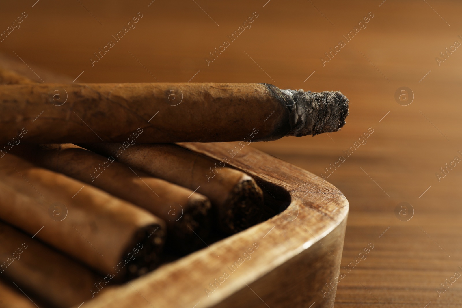 Photo of Many cigars in box on wooden table, closeup