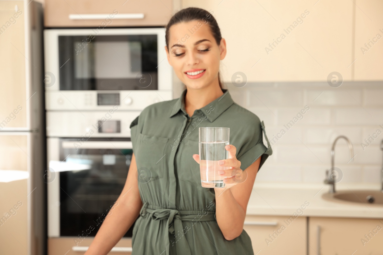 Photo of Young woman holding glass with water in kitchen