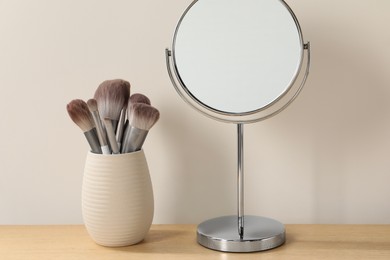 Mirror and makeup brushes on wooden dressing table in room