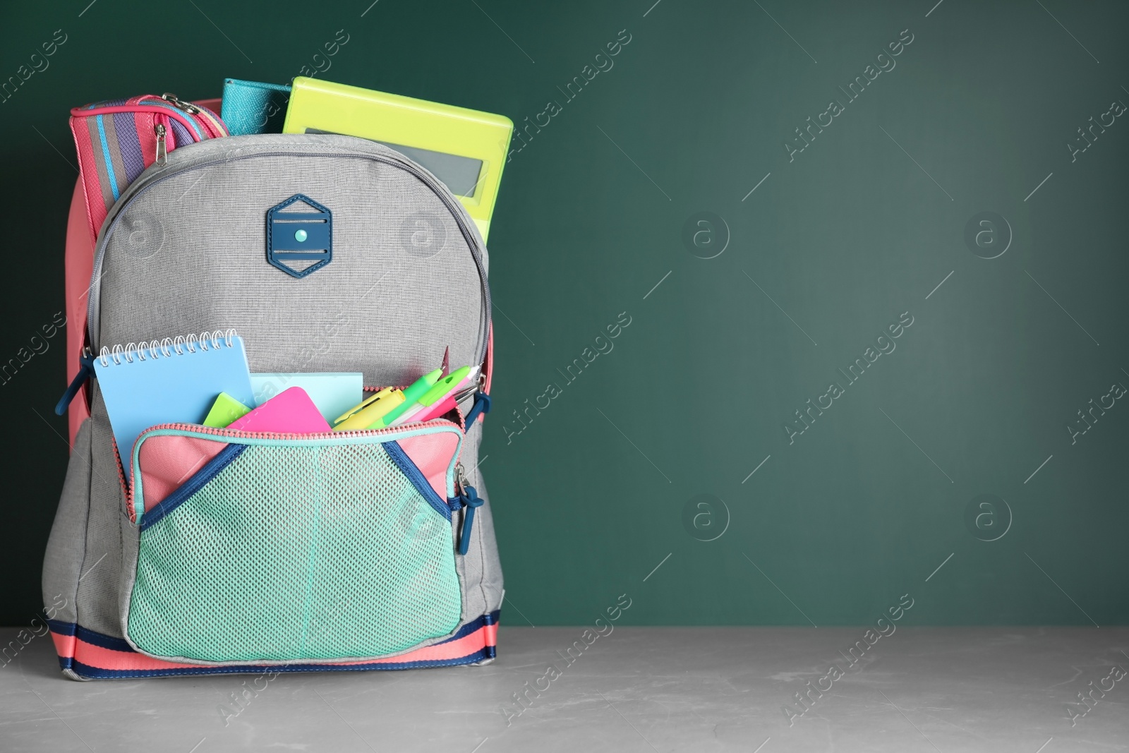 Photo of Stylish backpack with different school stationery on table against chalkboard. Space for text