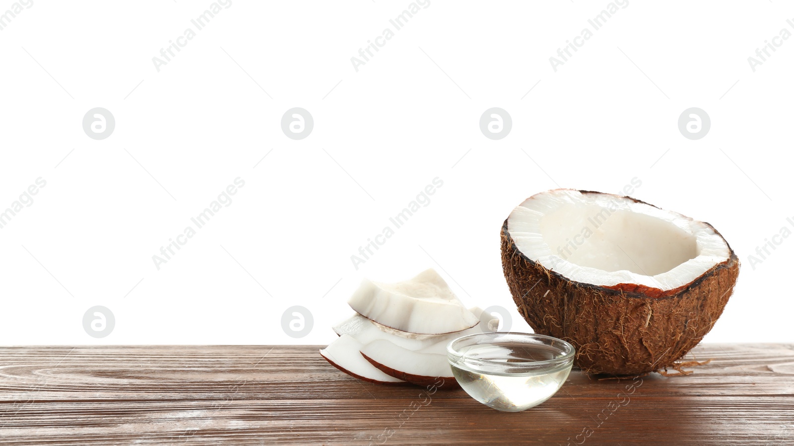 Photo of Ripe coconut and bowl with natural organic oil on wooden table against white background