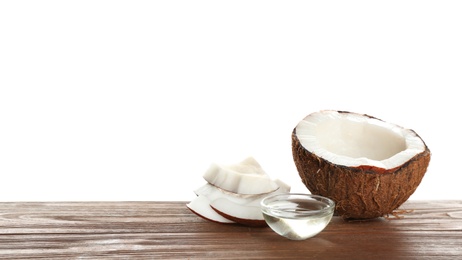 Ripe coconut and bowl with natural organic oil on wooden table against white background