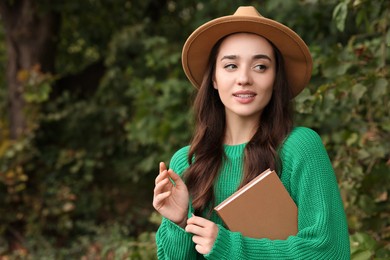 Photo of Beautiful young woman in stylish warm sweater with book outdoors, space for text