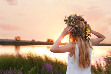 Photo of Young woman wearing wreath made of beautiful flowers outdoors at sunset