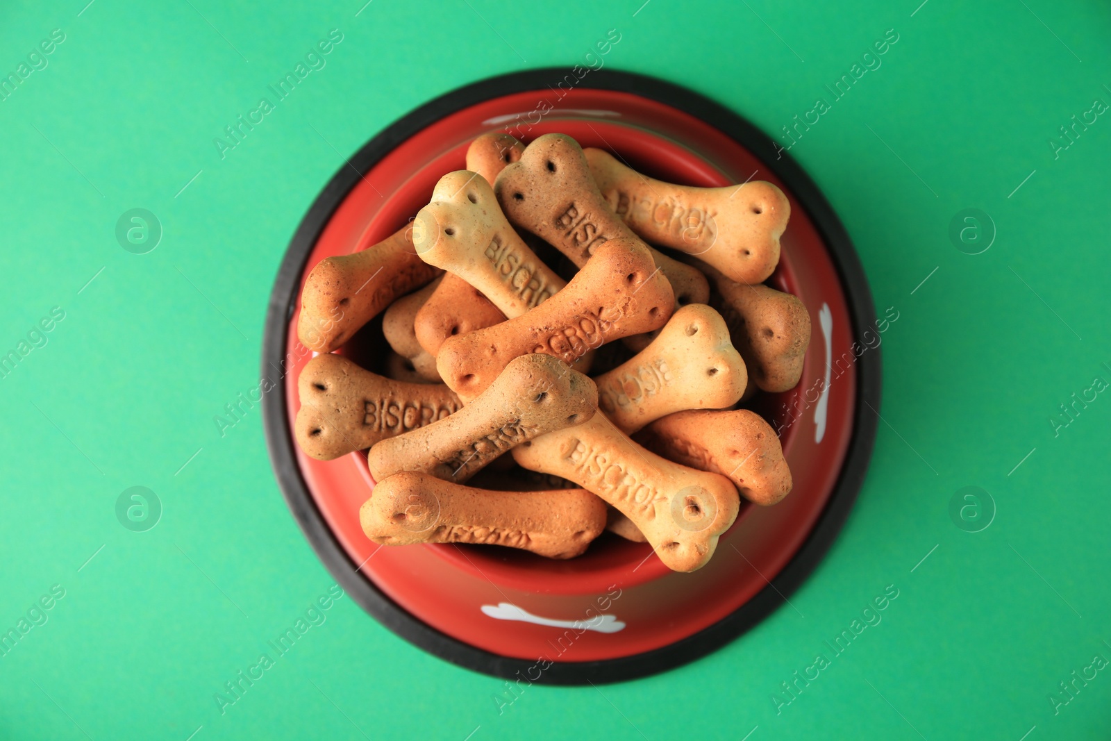 Photo of Bone shaped dog cookies in feeding bowl on green background, top view