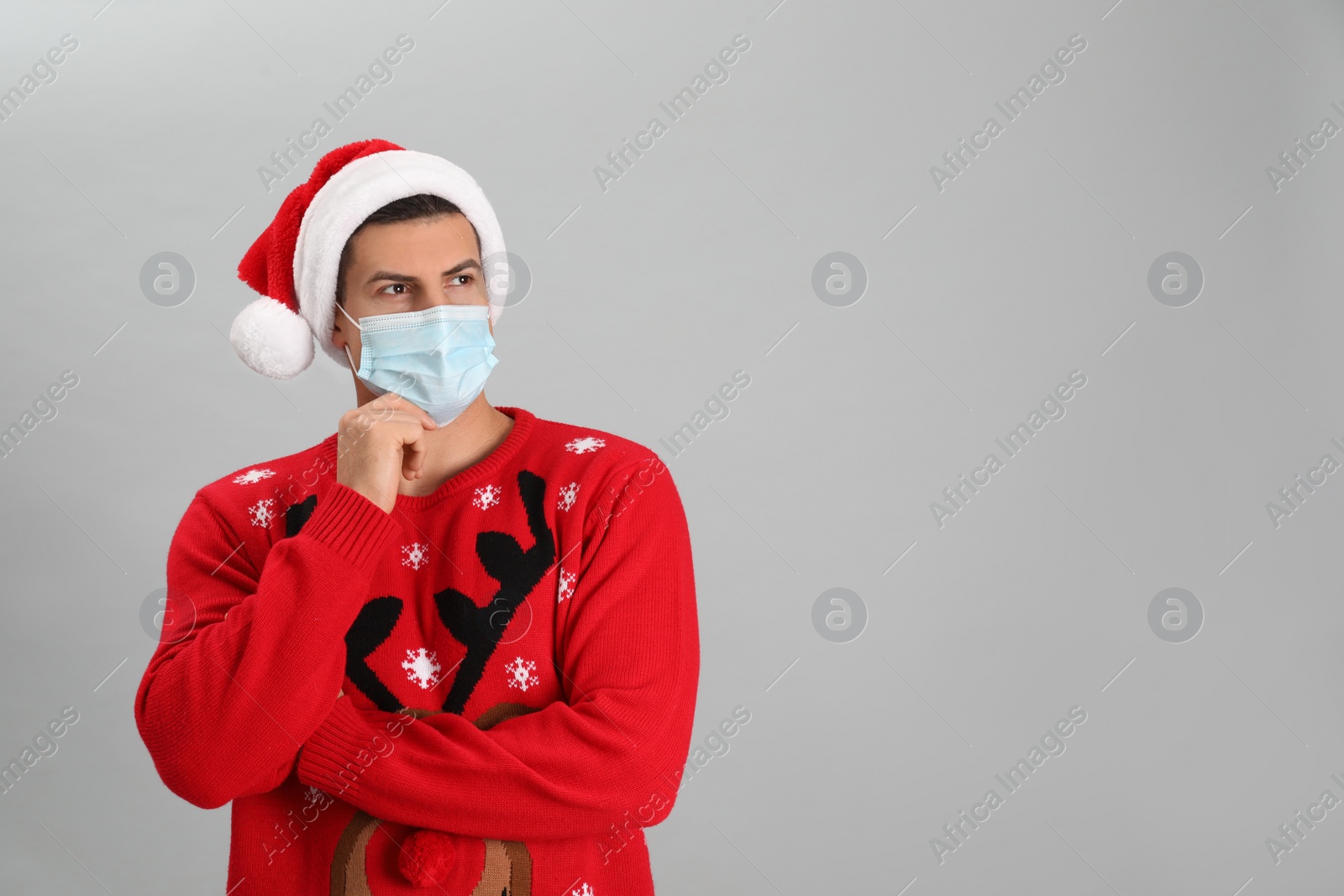 Photo of Man wearing Santa hat and medical mask on grey background, space for text