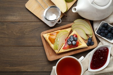 Fresh tasty puff pastry with jam, blueberries and pear served on wooden table, flat lay. Space for text