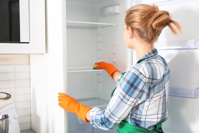 Woman in rubber gloves cleaning empty refrigerator at home