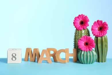 Photo of Composition with decorative cacti and flowers on table against color background, space for text. International Women's Day