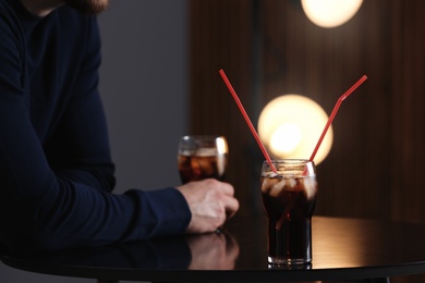 Glass of cola with ice on table against blurred background