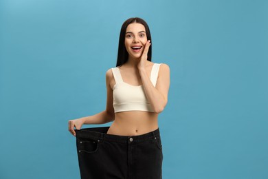 Photo of Happy young woman wearing big jeans after weight loss on turquoise background