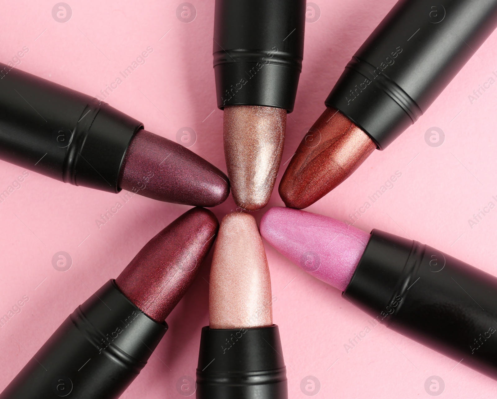 Photo of Set of bright lipsticks in black tubes on pink background, flat lay