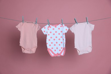 Photo of Baby clothes drying on laundry line against pink background