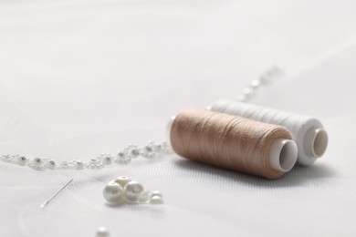 Photo of Spools of threads, needle and beads on white fabric, closeup. Space for text
