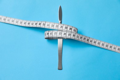 Photo of Scalpel and measuring tape on light blue background, top view. Weight loss surgery