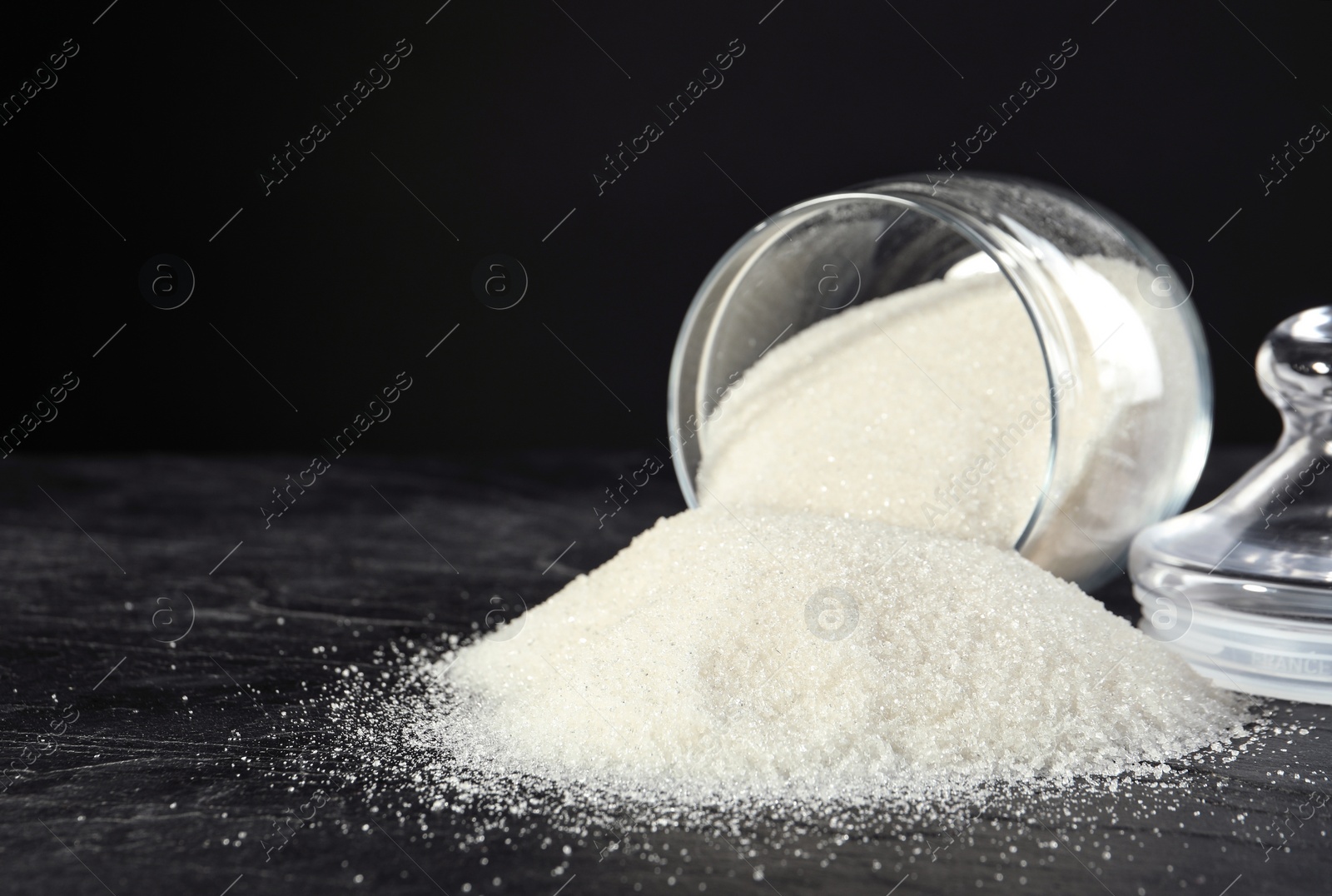 Photo of Overturned bowl with granulated sugar on black table