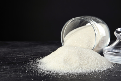 Photo of Overturned bowl with granulated sugar on black table