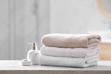 Photo of Clean towels, spa stones and soap dispenser on table in bathroom