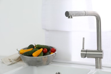 Modern sink with water tap and fresh vegetables near window in kitchen